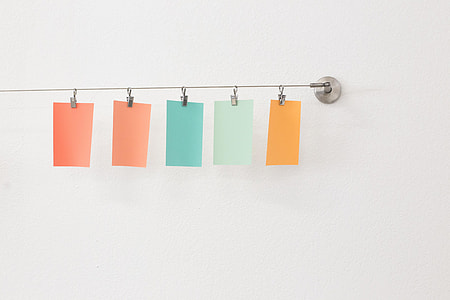 five assorted-color sticky notes hanged on gray wall hooks
