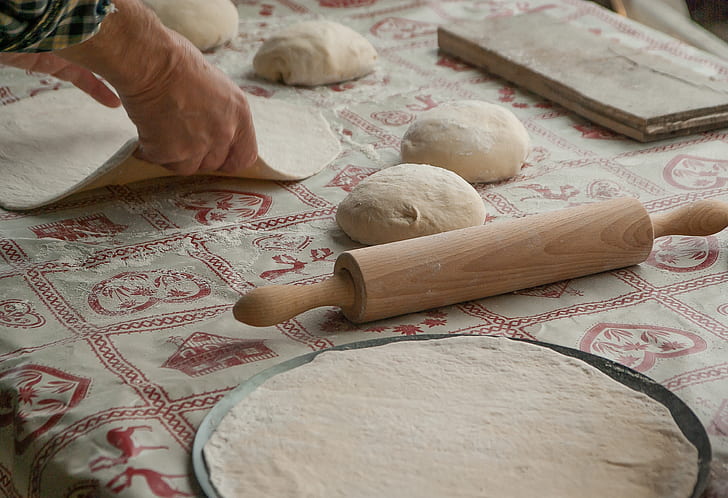 person holds dough near brown wooden rolling pin