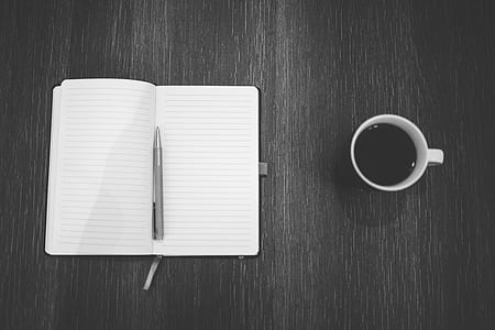 gray twist pen on notebook beside coffee filled mug