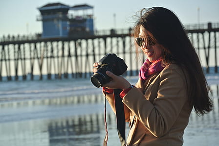 Selective Focus Photography of Woman Holding Her Camera Near Seashore