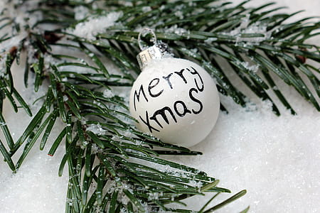 white Merry Xmas-printed bauble beside green leafed decor