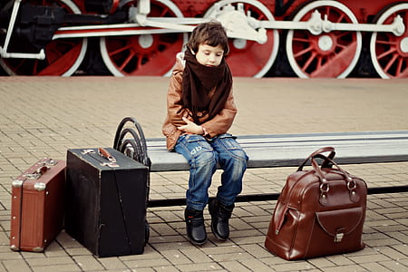 boy in brown jacket and blue jeans sitting on bench