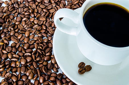 black coffee beans near white teacup on saucer