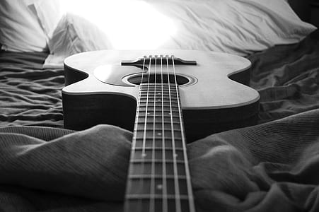 greyscale photo of acoustic guitar on bed