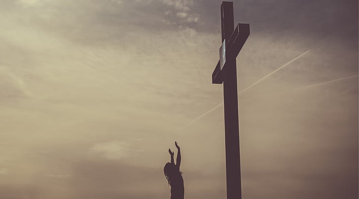 silhouette photography of person standing in front of cross
