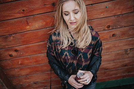 Blonde woman with a can of coke by a wooden wall
