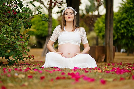 woman wearing white crop top and white skirt sitting on green grass with petals