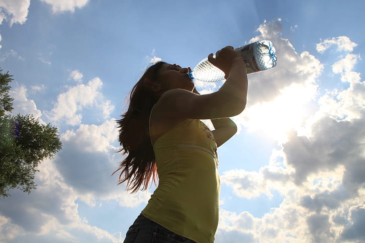 woman in yellow sleeveless top drinking water during daytime