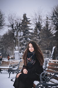 woman wearing black coat sitting on black and brown bench