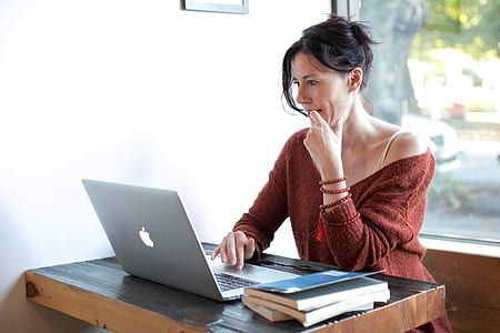 woman touching chin while scrolling through the laptop