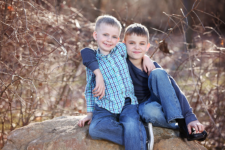 two boy dressed sitting on a big rock