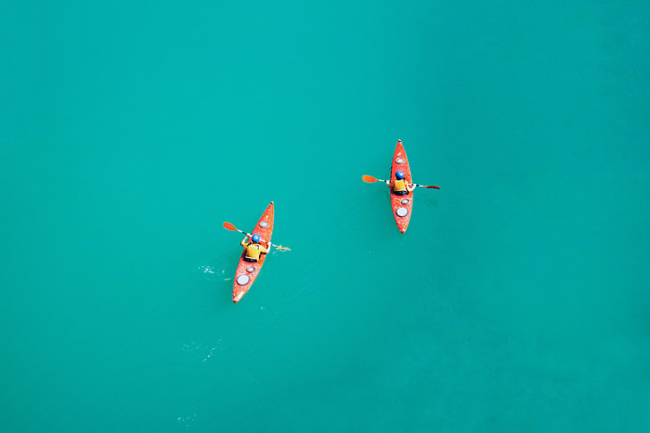 two person riding on red kayak with paddles
