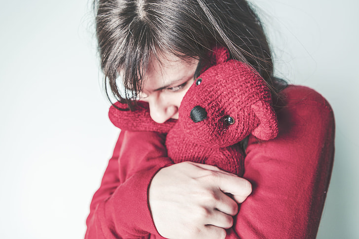 person wearing red sweat shirt and hugging bear plush toy