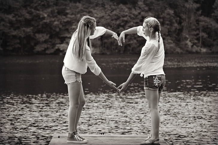 grayscale photo of two woman doing heart sign