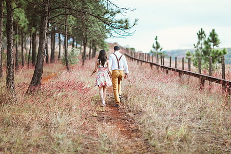 man wearing white dress shirt holding woman's hand walking on flower field