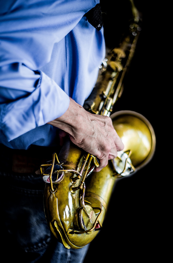 person wearing blue dress shirt playing brass saxophone