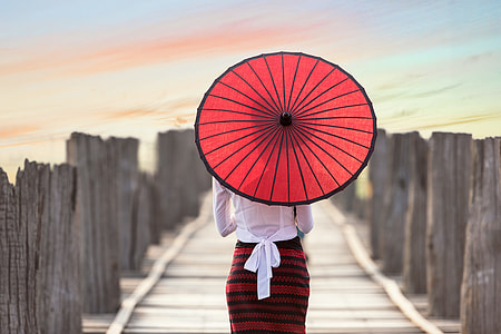 woman in white and red dress using paper umbrella at dock during daytime