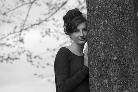 grayscale photography of woman hiding on tree trunk