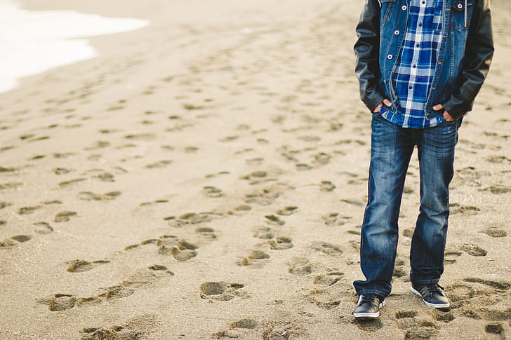man wearing faded jeans standing on sand