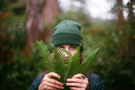 woman wearing green knit cap and black top holding green fern plant in selective focus photography