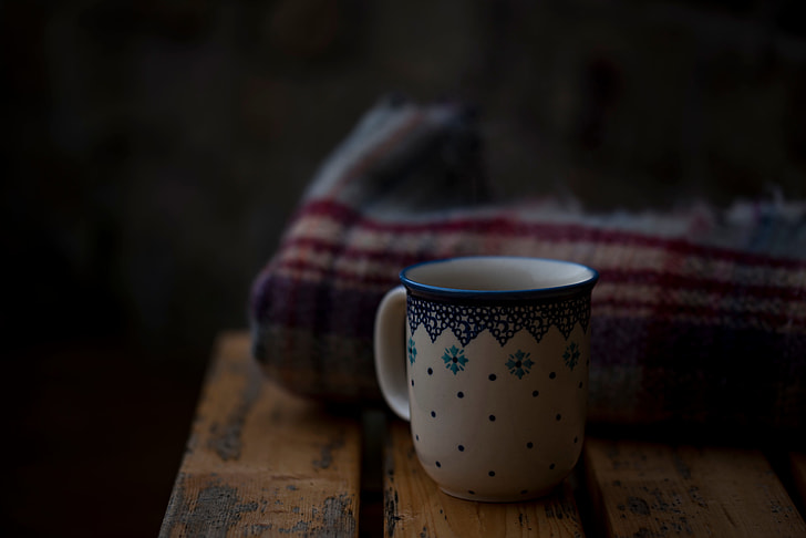white and blue ceramic mug in front of beige and red textile