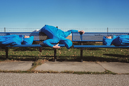 photo of three person wearing blue hoodies laying in blue metal bench