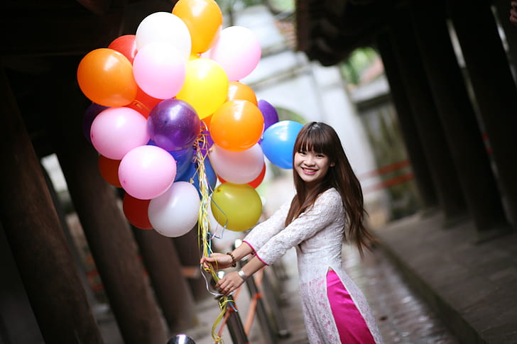 woman in white dress holding assorted-color bundle of balloons