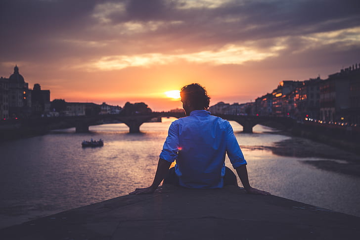 silhouette of man sitting front of bridge during golden hour