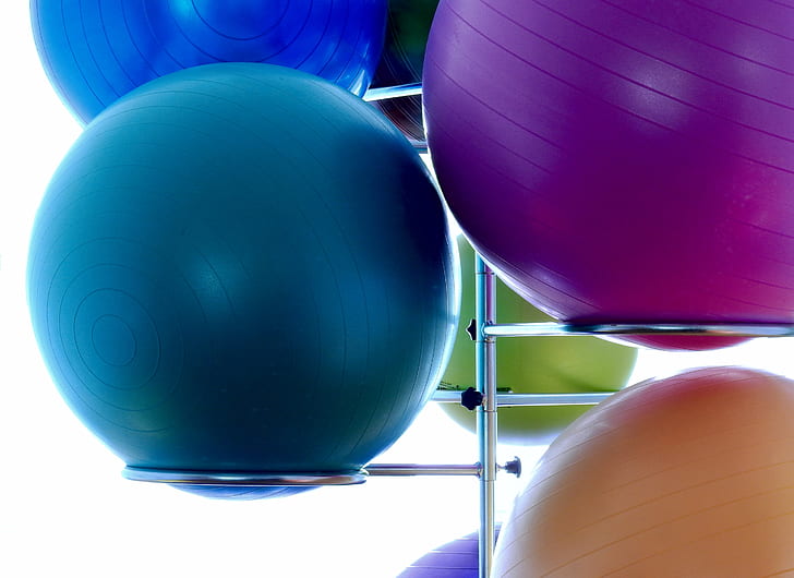 two blue, one purple, and one orange stability balls on stainless steel rack