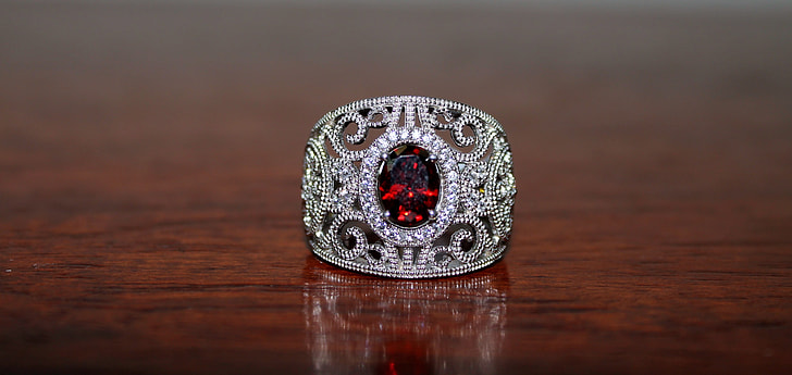 silver-colored ring with red gemstone on brown wooden surface