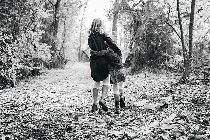 two girls walking on leaf-covered road in forest
