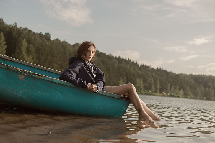 woman in black jacket sitting on green boat near trees during daytime