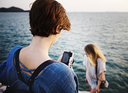 woman holding camera facing woman standing near on water