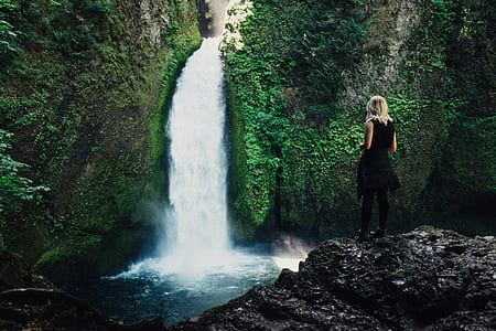 woman wearing black sleeveless dress standing in front of waterfalls