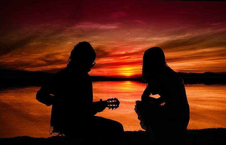 silhouette of two people sitting on ground during sunset
