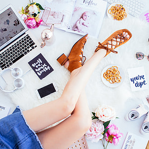 woman sitting on rug surrounded with laptop, flowers, art materials, and shoes flatlay photography