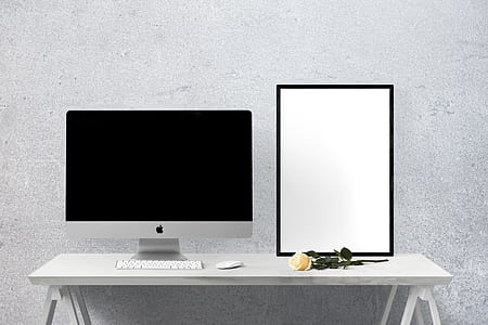 silver iMac on table beside yellow rose