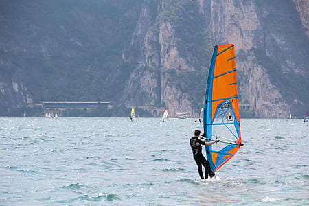 Man in Black Wetsuit Standing on Orange and Blue Sailboat during Daytime