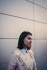 woman in beige jacket standing near wall