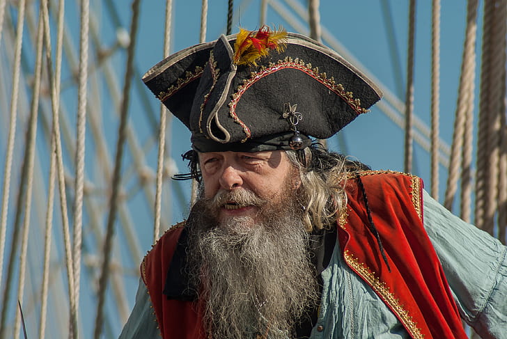 man wearing black pirate hat, red vest, and blue shirt on front of ropes