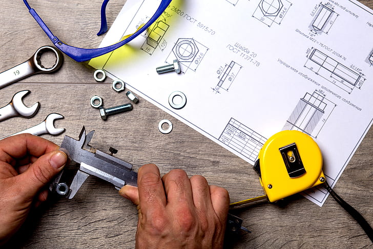 person holding black metal handheld tool in front of sketch paper