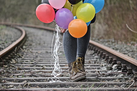 selective focus photography of person walking on train rail while holding balloons