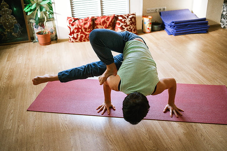 person in green sleeveless shirt doing yoga on red yoga mat