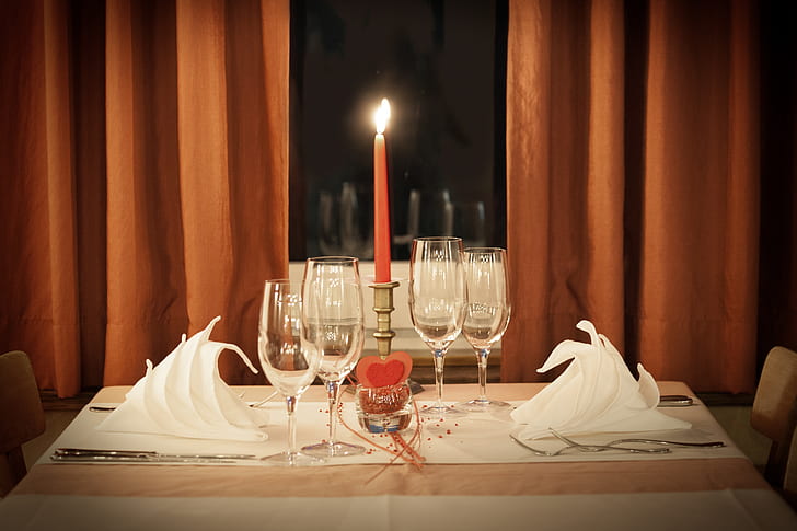 four clear flute glasses on table beside red taper candle