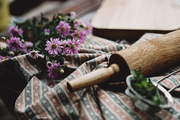 pink Asters flowers near brown wooden rolling pin