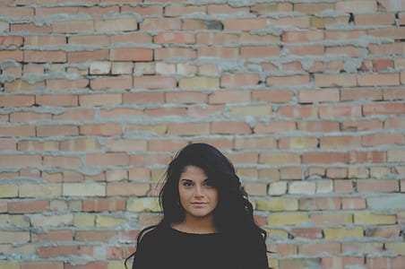 woman wears black top standing beside brown bricked wall