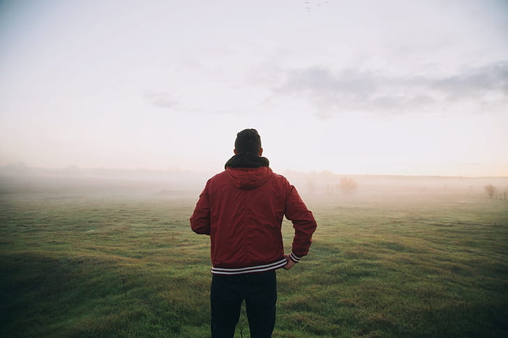 man in red full-zip jacket on green grass field during foggy day