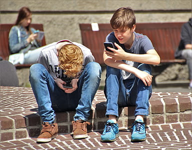 two boy sitting on brown brick pavement taken during daytime