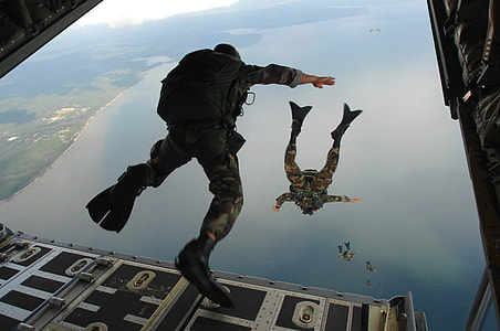 men in military uniform skydiving on sea during daytime