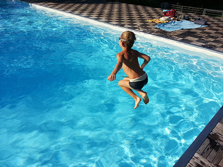 boy jumping on swimming pool during daytime